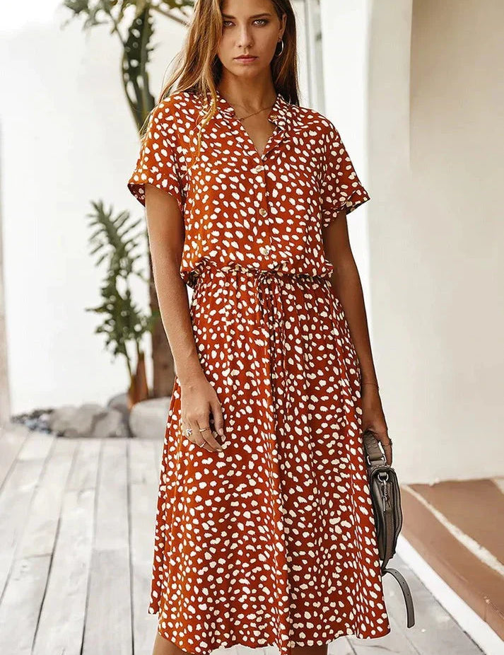 Abito estivo donna a pois bianchi su sfondo arancione, maniche corte, lunghezza media, cintura in vita, moda casual, perfetto per giornate calde.