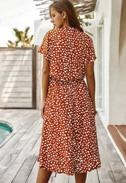 Donna con abito estivo a pois bianchi su sfondo rosso, in piedi su terrazza in legno vicino a piscina. Moda femminile, abbigliamento casual elegante.