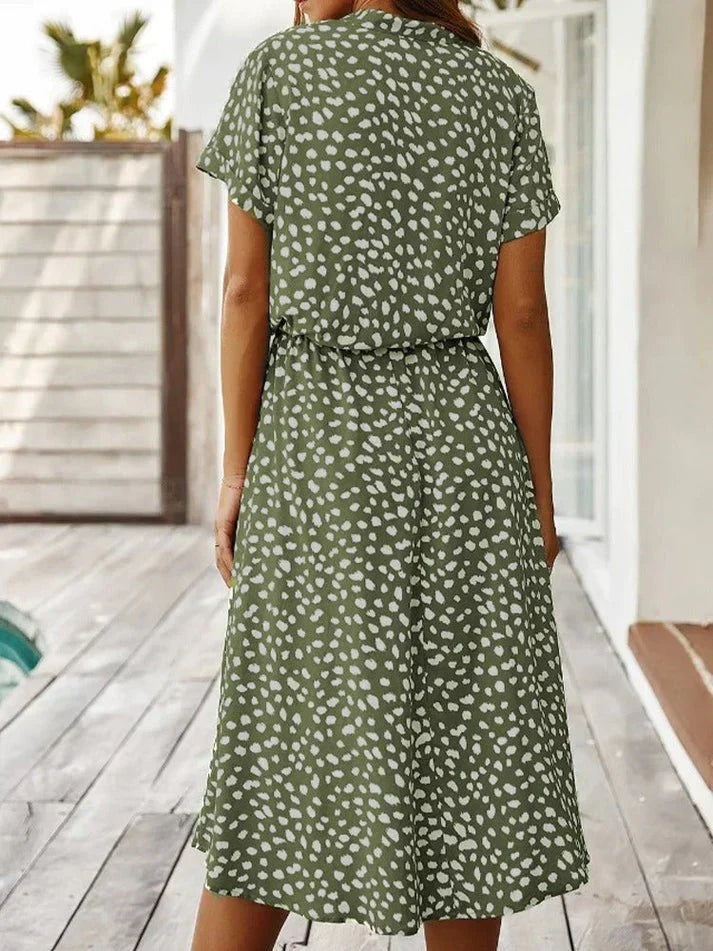 Abito estivo verde a pois bianchi, maniche corte, lunghezza media, indossato da donna su terrazza. Moda casual, abbigliamento femminile elegante.