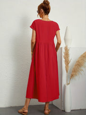 Donna con abito lungo rosso, sandali beige, accanto a vaso bianco con pampas. Moda estiva, abbigliamento casual elegante, tendenze 2023.