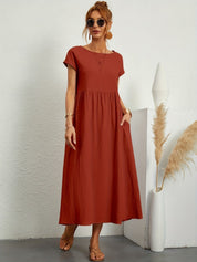 Donna con abito lungo rosso, occhiali da sole, sandali, accanto a vaso bianco con pampas. Moda estiva elegante, abbigliamento casual chic.