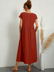 Donna con abito lungo rosso terracotta, sandali beige, vaso bianco con pampas. Moda estiva, abbigliamento casual elegante.