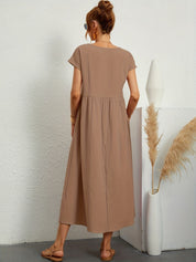 Abito lungo marrone chiaro, donna di spalle, sandali beige, vaso bianco con pampas, moda estiva casual, abbigliamento femminile elegante.
