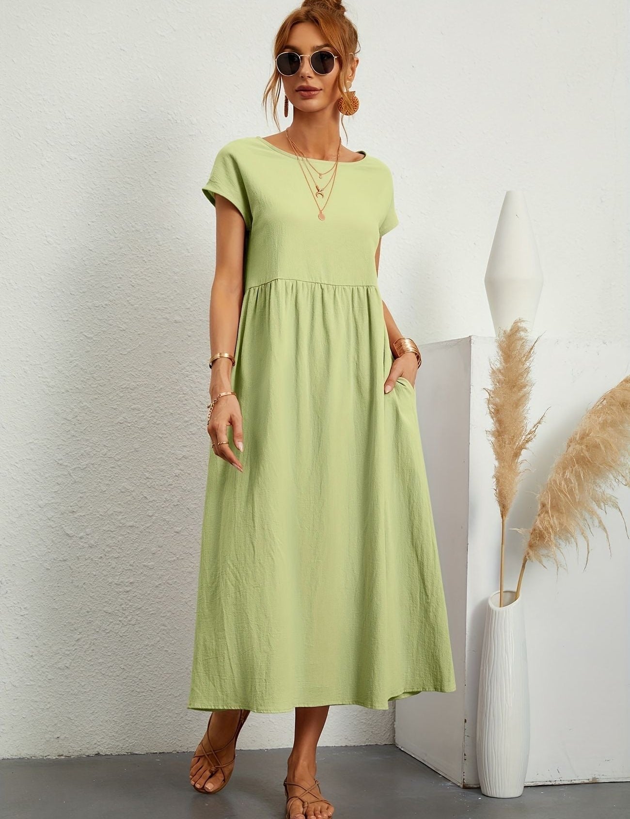 Abito lungo verde chiaro estivo, donna con occhiali da sole, sandali, accessori dorati, sfondo bianco minimalista, moda casual elegante.