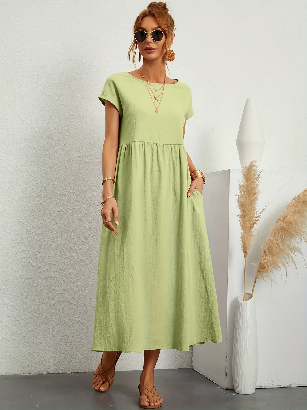 Abito lungo verde chiaro estivo, donna con occhiali da sole, sandali, accessori dorati, sfondo bianco minimalista, moda casual elegante.