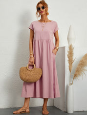 Donna con abito lungo rosa, borsa di paglia, sandali beige, occhiali da sole. Sfondo bianco con decorazioni minimaliste. Moda estiva elegante.