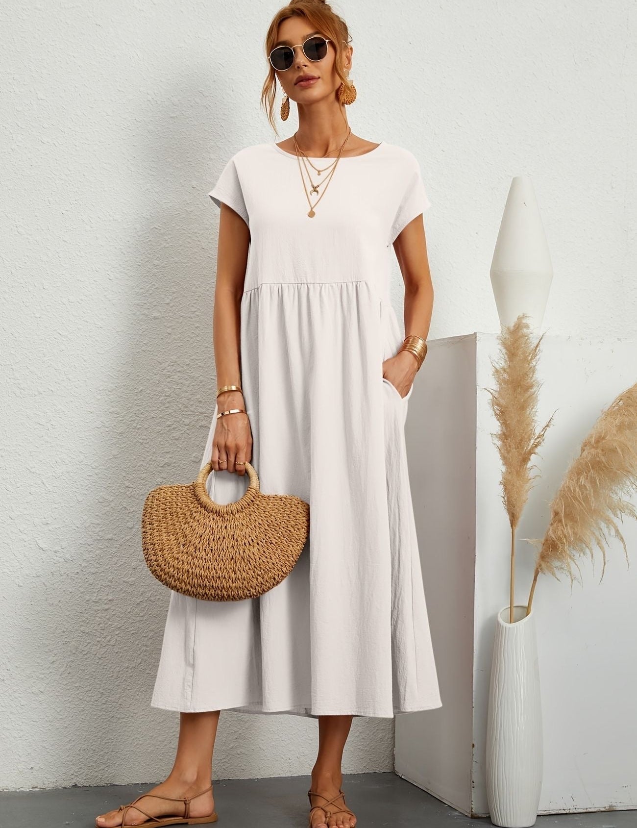 Donna con abito bianco estivo, borsa di paglia, sandali, occhiali da sole. Moda casual elegante, accessori dorati, sfondo neutro.