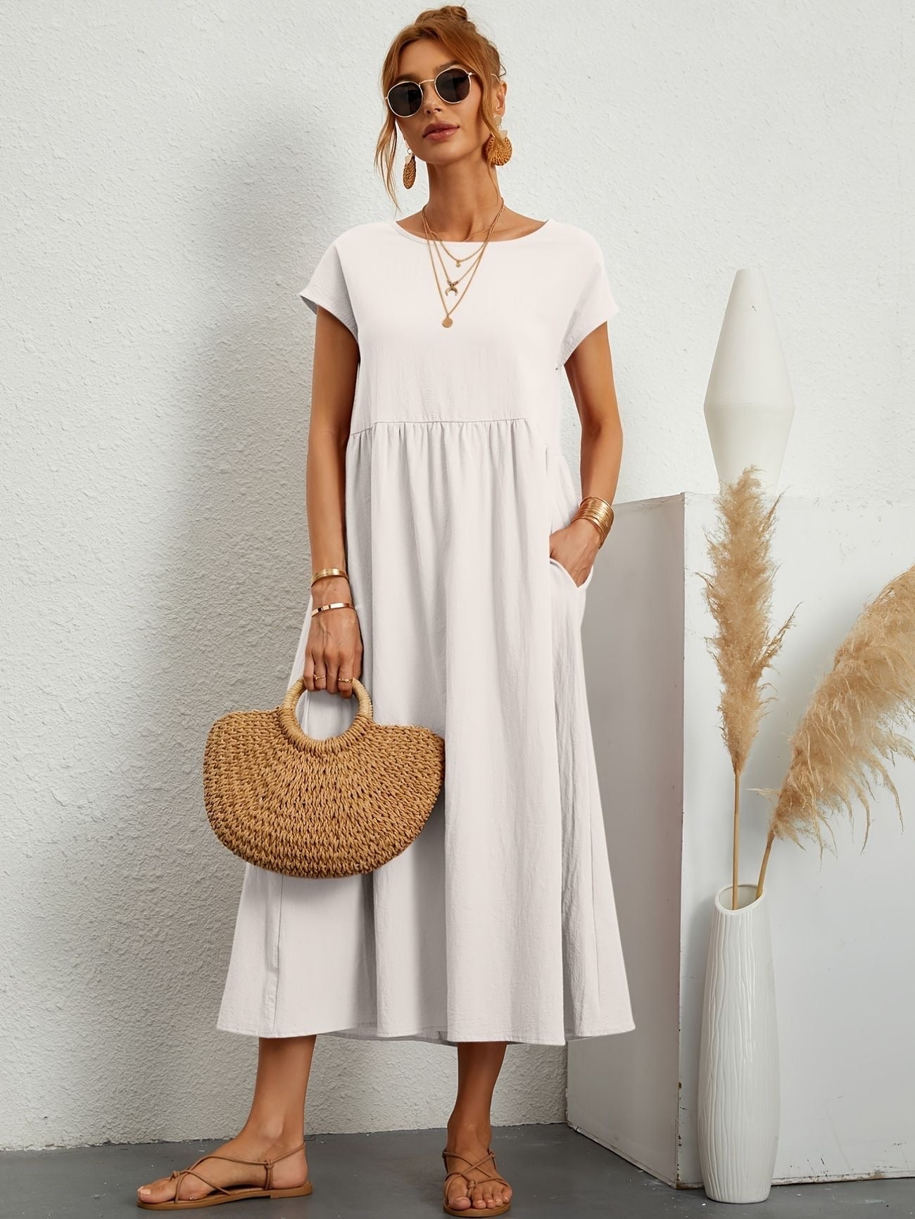 Donna con abito bianco estivo, borsa di paglia, sandali, occhiali da sole. Moda casual elegante, accessori dorati, sfondo neutro.