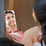 Donna che usa uno specchio portatile illuminato con set di pennelli da trucco rosa. Accessorio cosmetico ideale per trucco preciso e portatile.