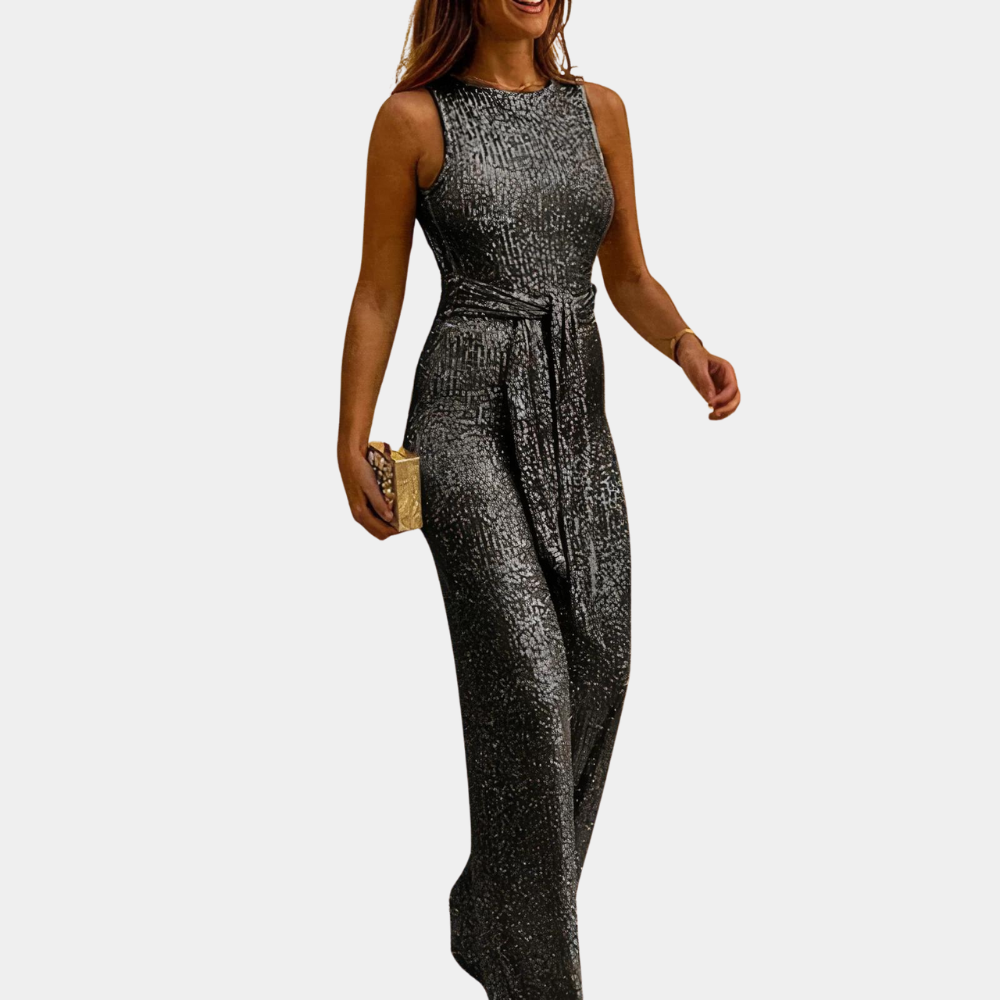 Donna in abito lungo argento scintillante, senza maniche, con cintura in vita, tiene una pochette dorata. Moda elegante da sera.