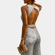 Donna in tuta argento scintillante con schiena scoperta, clutch dorata, orologio elegante. Moda serale glamour, abbigliamento da festa.