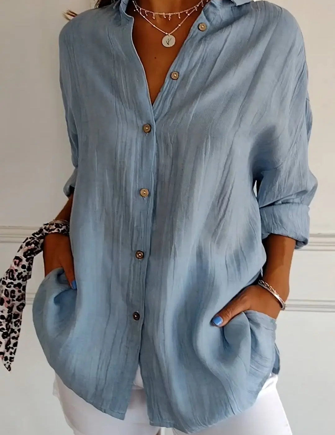 Camicia donna azzurra in lino con bottoni, maniche lunghe arrotolate, abbinata a pantaloni bianchi. Stile casual elegante, moda estiva.