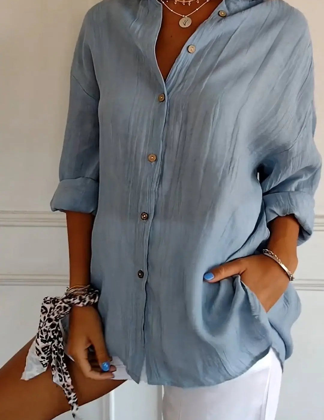 Camicia donna azzurra in lino con bottoni, maniche lunghe arrotolate, abbinata a pantaloncini bianchi. Look estivo casual ed elegante.