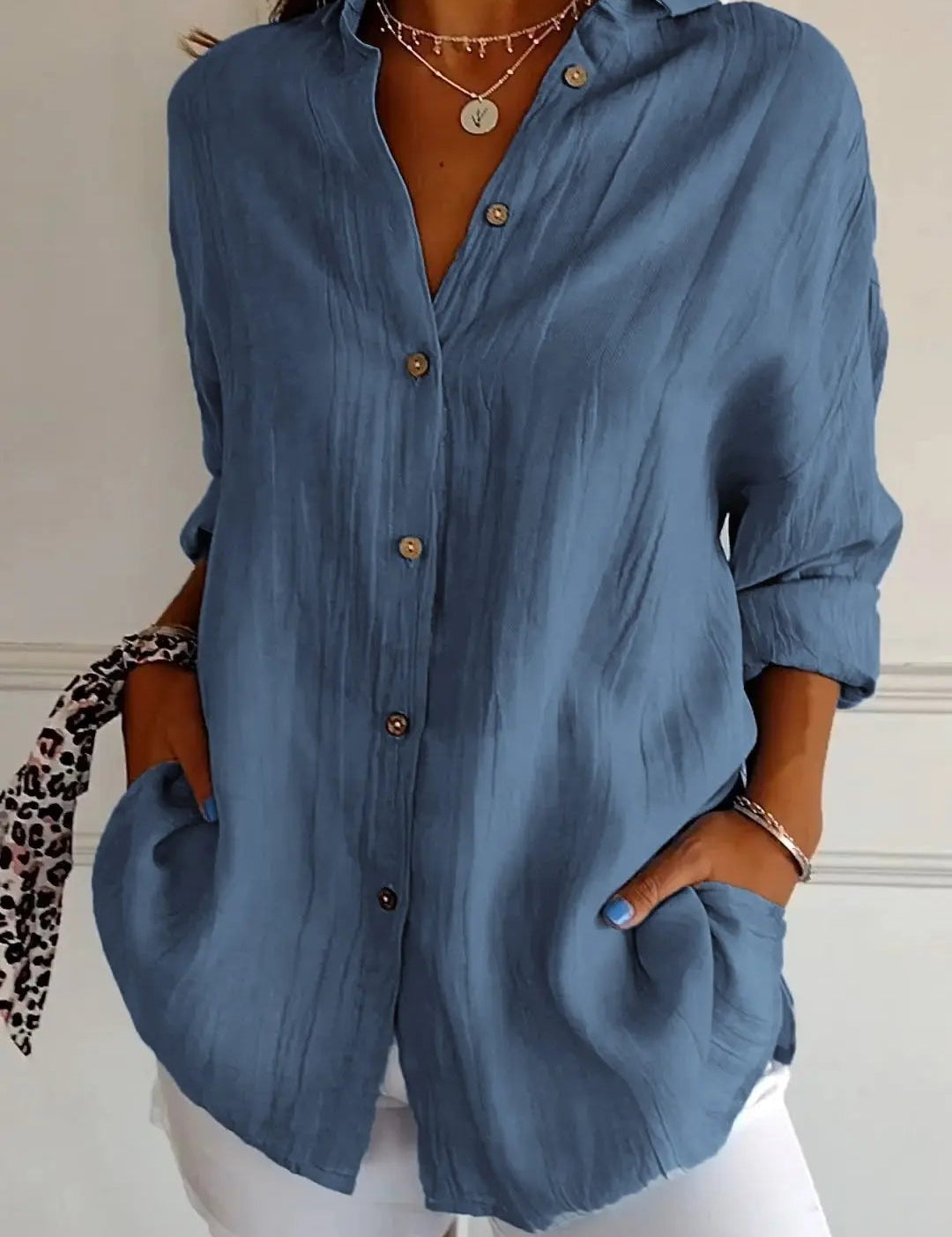 Camicia donna blu a maniche lunghe con bottoni, stile casual, abbinata a pantaloni bianchi. Accessori: collana e bracciale. Moda femminile elegante.