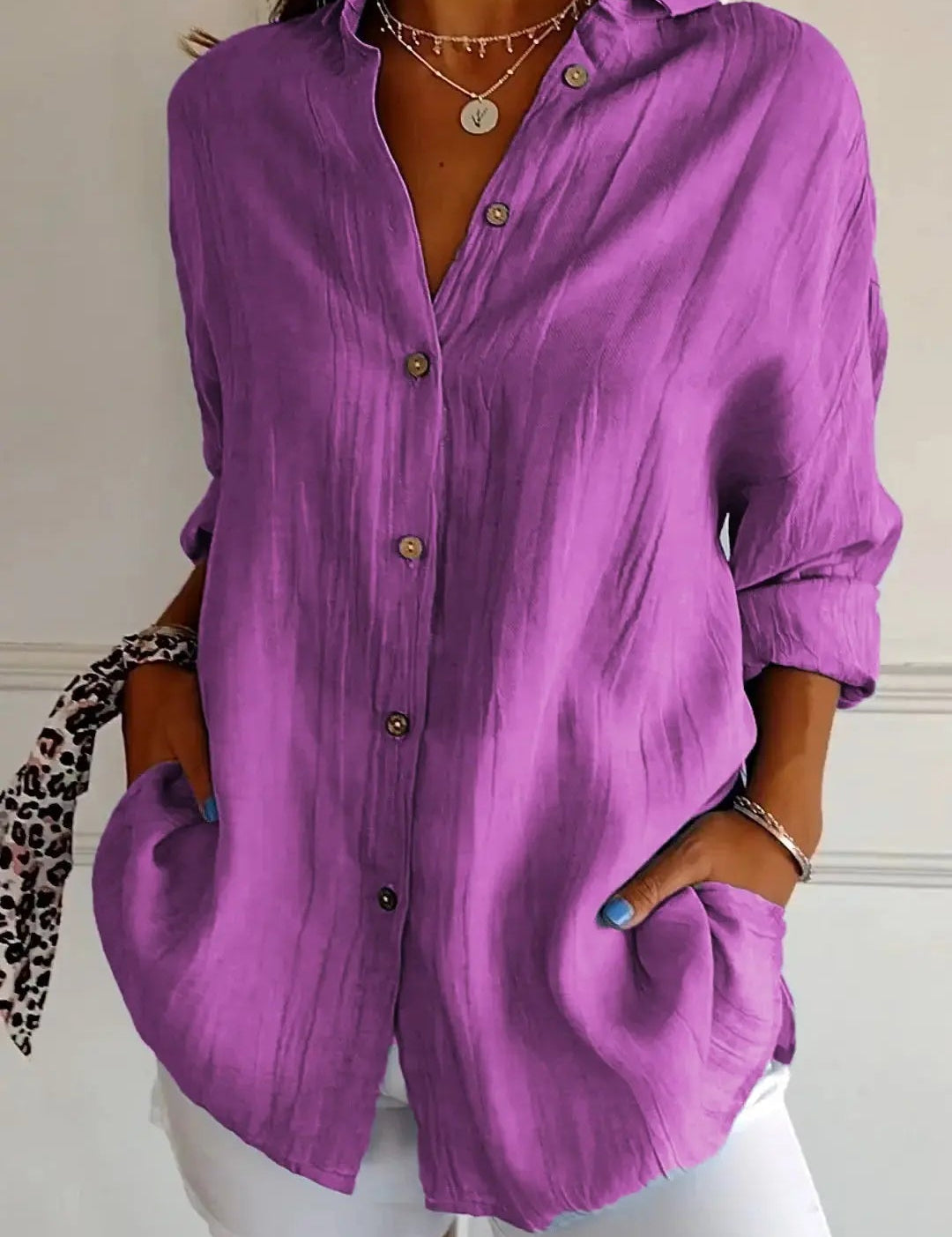 Camicia viola da donna in lino, maniche lunghe, bottoni frontali, tasche laterali, abbinata a pantaloni bianchi. Stile casual elegante.