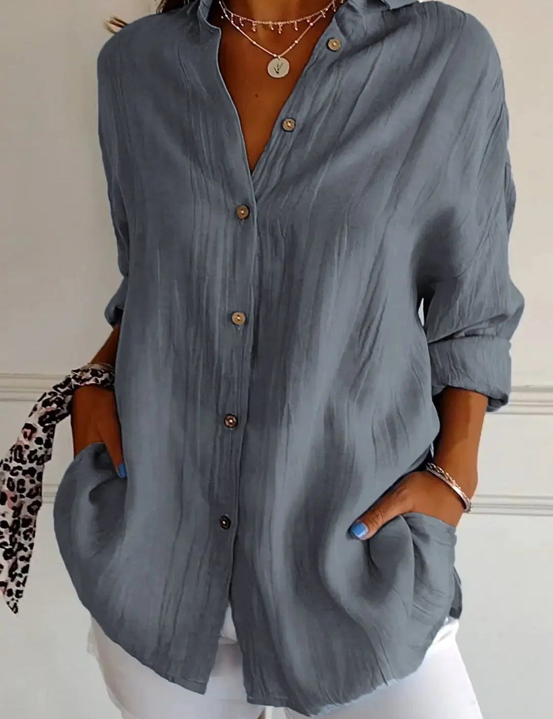 Camicia donna grigia a maniche lunghe, bottoni in legno, tasche frontali, abbinata a pantaloni bianchi. Stile casual elegante, moda femminile.