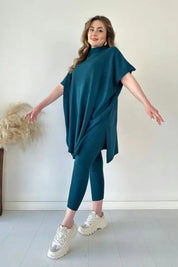 Modella indossa completo maglia oversize blu petrolio e leggings coordinati, scarpe da ginnastica bianche. Moda donna casual, abbigliamento comodo.