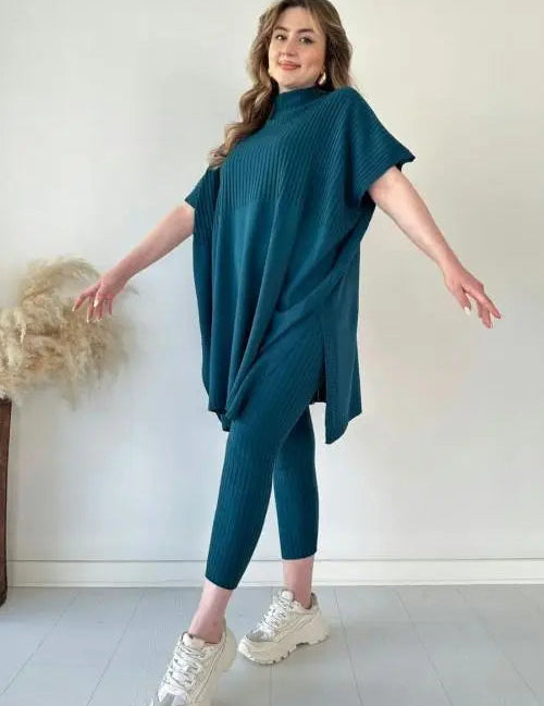 Modella indossa completo maglia oversize blu petrolio e leggings coordinati, scarpe da ginnastica bianche. Moda donna casual, abbigliamento comodo.