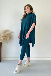Donna in abbigliamento casual elegante, indossa un completo blu petrolio con maglia oversize e leggings, scarpe da ginnastica bianche.