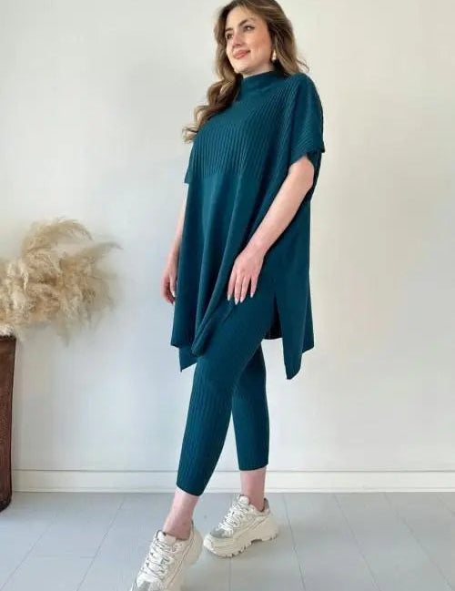 Donna in abbigliamento casual elegante, indossa un completo blu petrolio con maglia oversize e leggings, scarpe da ginnastica bianche.