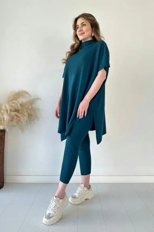 Donna in abbigliamento casual elegante, indossa un completo blu petrolio con maglia oversize e leggings, scarpe da ginnastica bianche.