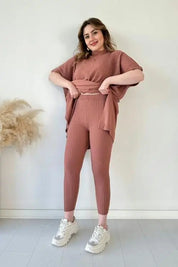 Donna in completo coordinato maglia rosa, pantaloni e maglia a maniche corte, posa sorridente. Moda donna, abbigliamento casual elegante.