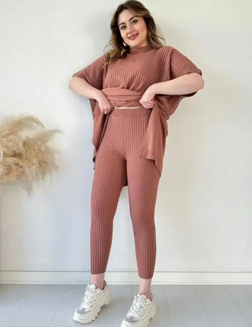 Donna in completo coordinato maglia rosa, pantaloni e maglia a maniche corte, posa sorridente. Moda donna, abbigliamento casual elegante.