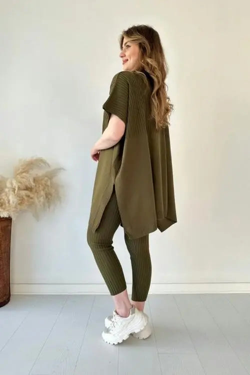 Donna in abbigliamento casual verde oliva, maglia oversize e leggings a coste, scarpe da ginnastica bianche. Sfondo neutro, stile moderno.