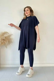Donna in abito tunica blu scuro e leggings coordinati, scarpe da ginnastica bianche, posa su sfondo neutro. Moda casual, abbigliamento donna elegante.