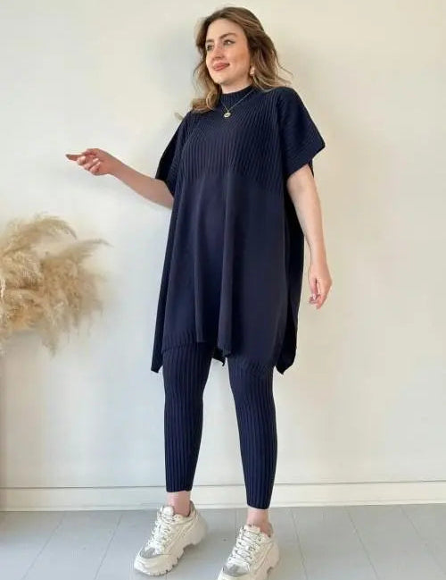 Donna in abito tunica blu scuro e leggings coordinati, scarpe da ginnastica bianche, posa su sfondo neutro. Moda casual, abbigliamento donna elegante.