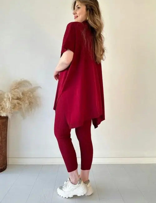 Donna in abbigliamento casual rosso, maglia oversize e leggings, scarpe da ginnastica bianche, sfondo neutro, moda femminile autunnale.