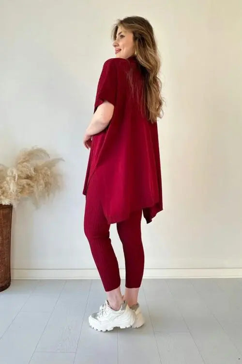 Donna in abbigliamento casual rosso, maglia oversize e leggings, scarpe da ginnastica bianche, sfondo neutro, moda femminile autunnale.
