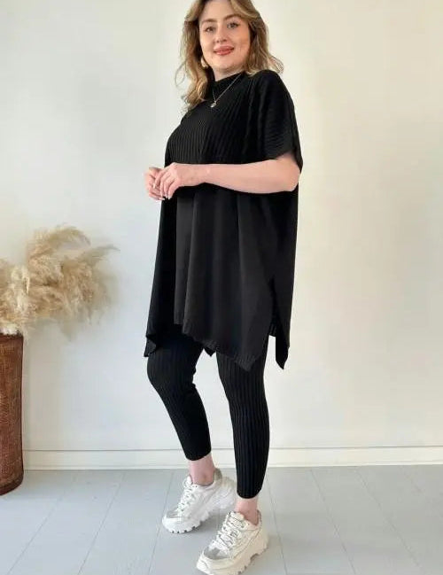 Donna in abbigliamento casual nero, maglia oversize e leggings, scarpe da ginnastica bianche, sfondo neutro. Moda donna, outfit comodo.