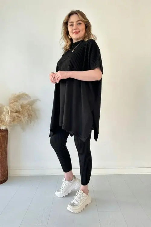 Donna in abbigliamento casual nero, maglia oversize e leggings, scarpe da ginnastica bianche, sfondo neutro. Moda donna, outfit comodo.