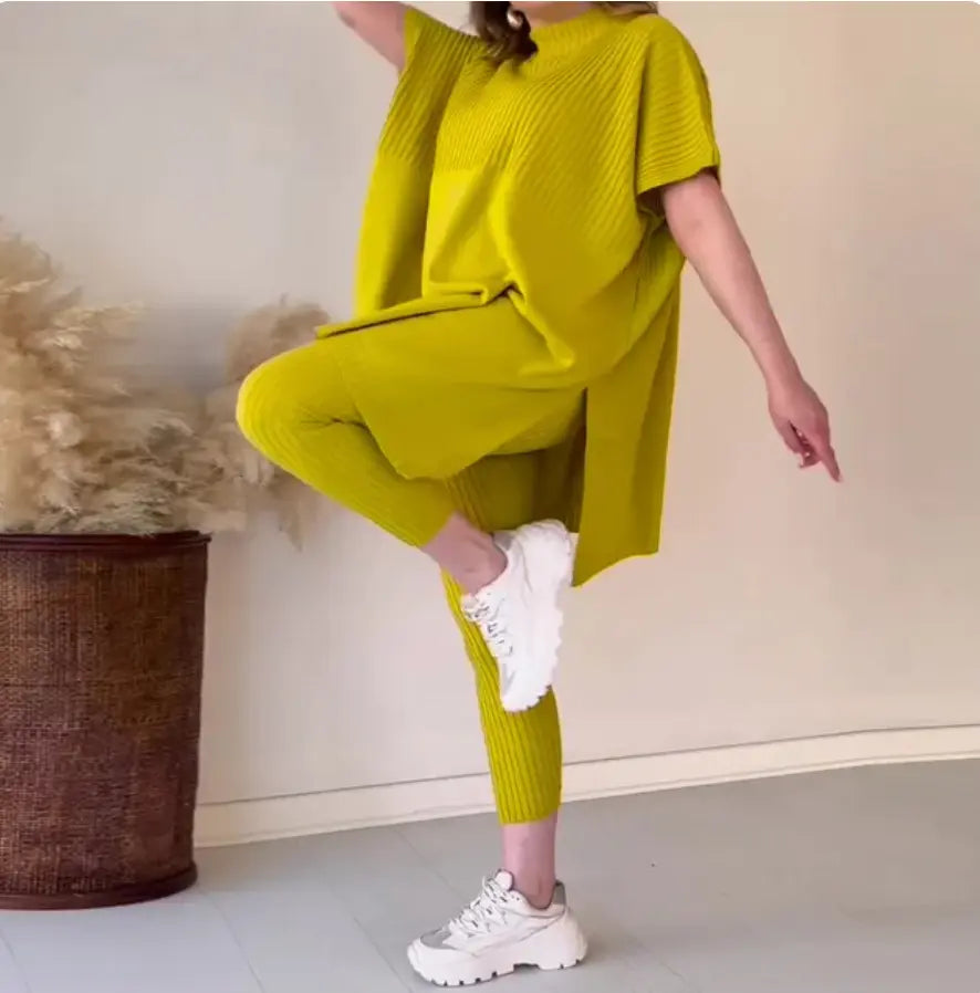 Donna in abbigliamento sportivo giallo lime, posa yoga, leggings e maglia oversize, scarpe da ginnastica bianche, sfondo neutro.