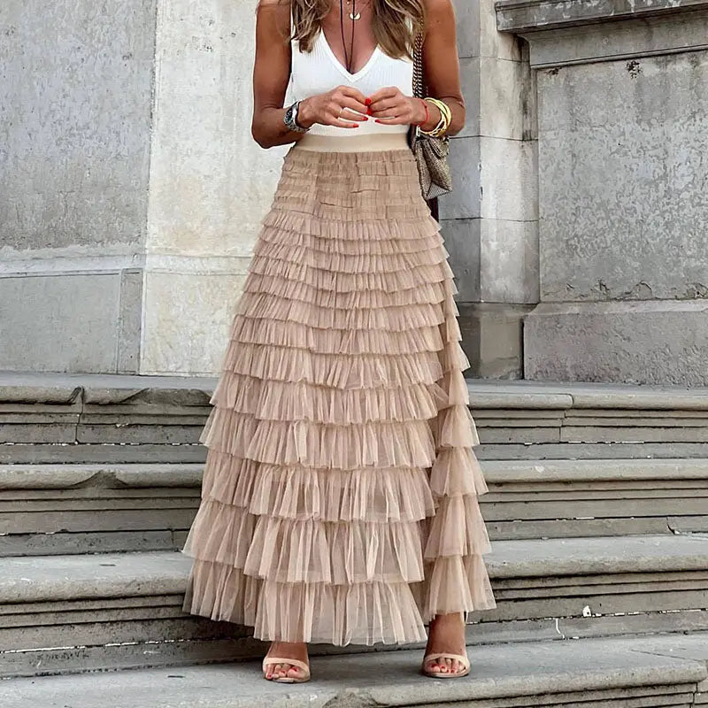 Donna con gonna lunga a balze beige, top bianco senza maniche, sandali, su gradini di pietra. Moda estiva elegante, abbigliamento femminile chic.