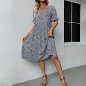 Vestito estivo donna a fiori blu e bianchi, maniche corte, lunghezza al ginocchio, indossato con sandali neri. Moda casual elegante.