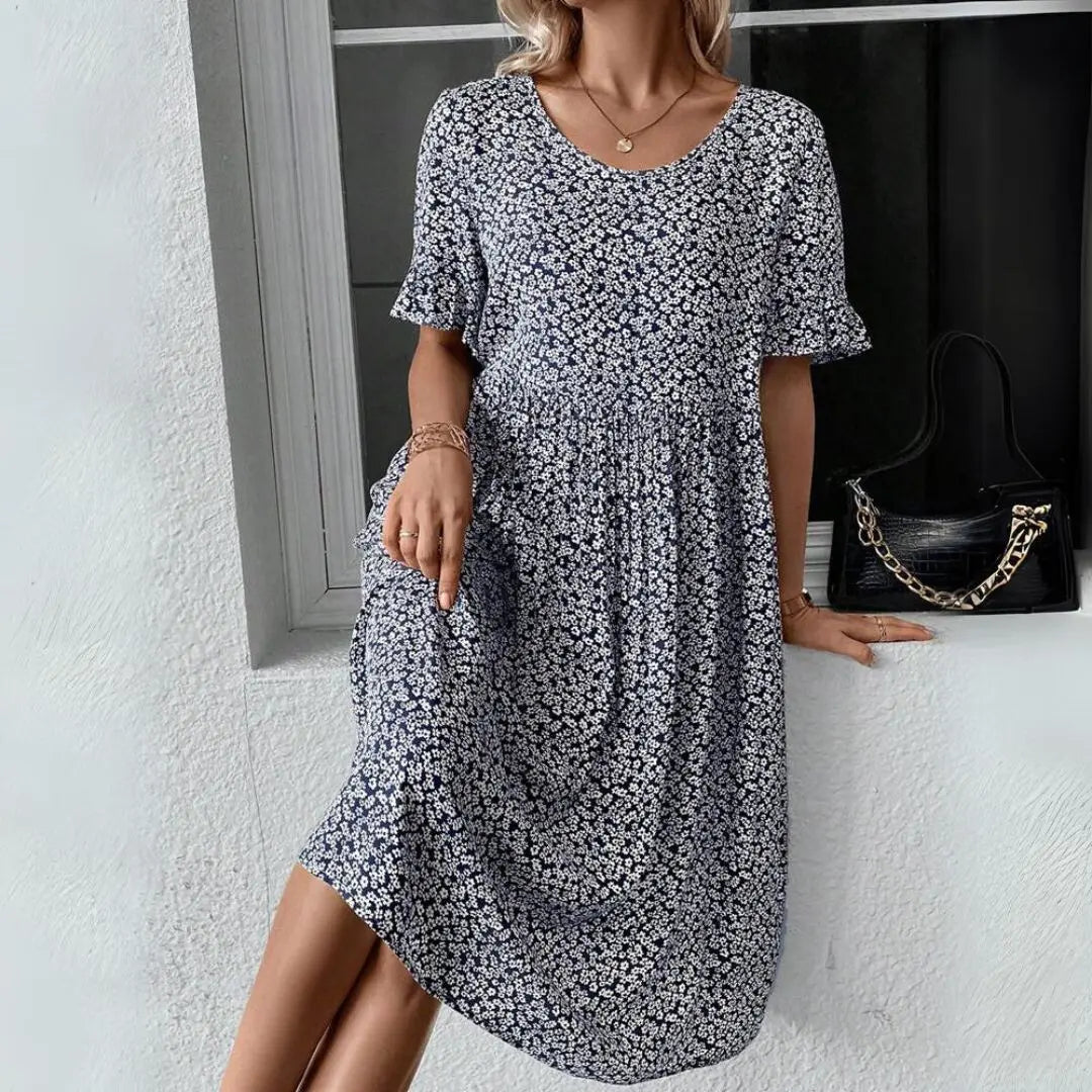 Abito estivo donna floreale blu, maniche corte, scollo rotondo, tessuto leggero, perfetto per look casual. Accessori: borsa nera con catena.