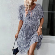 Donna con abito estivo floreale blu, maniche corte, orologio oro, borsa nera. Moda femminile casual, look estivo elegante.