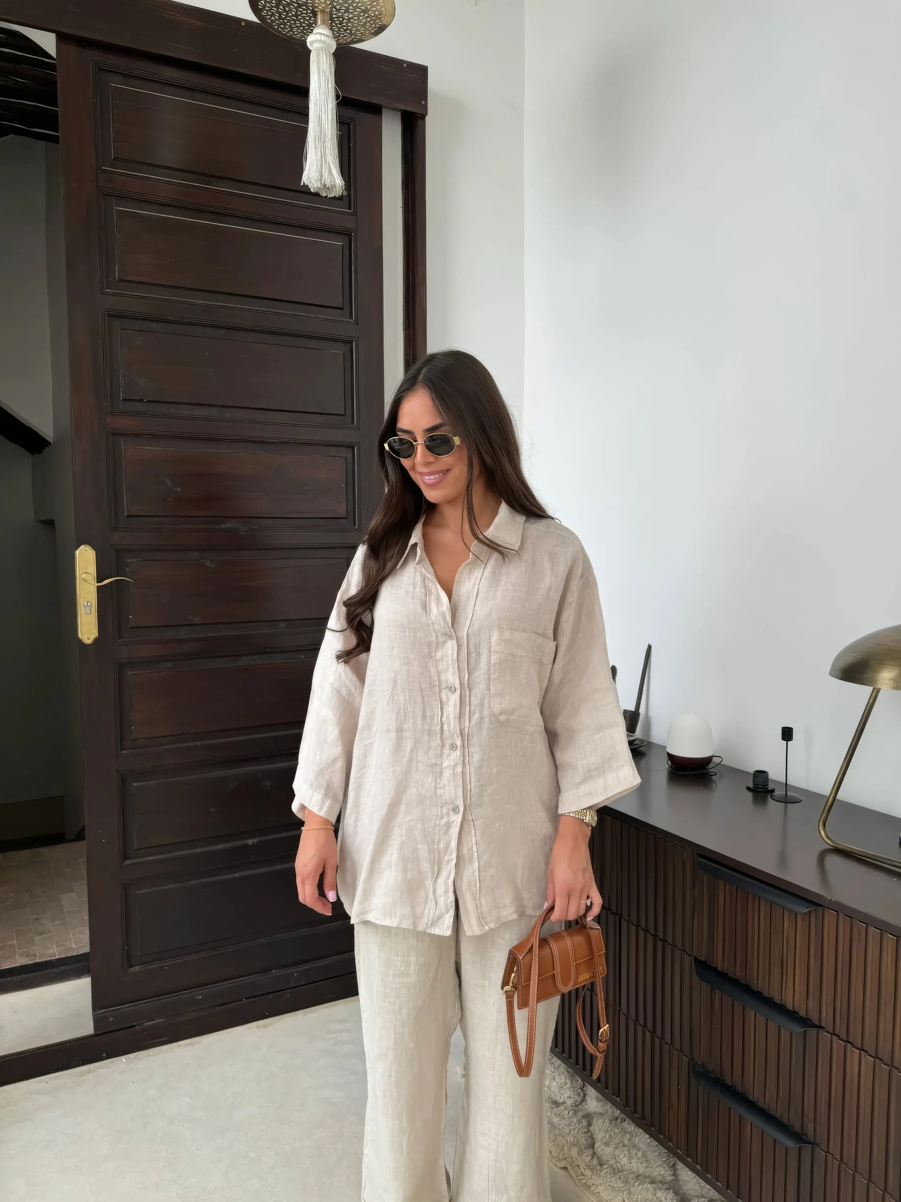 Donna con camicia di lino beige, pantaloni coordinati, occhiali da sole e borsa marrone. Look estivo elegante, moda femminile casual chic.