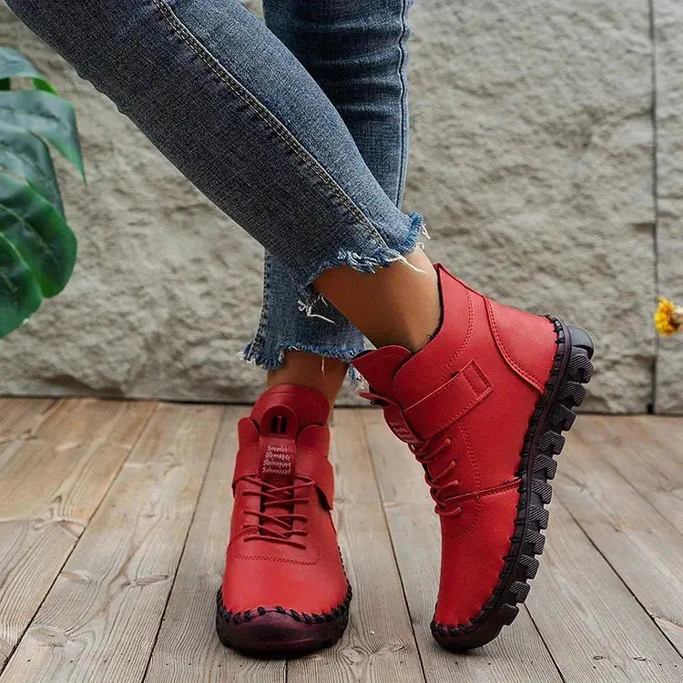 Scarpe da donna rosse in pelle, stivaletti casual con suola antiscivolo nera, indossati con jeans strappati su pavimento in legno.