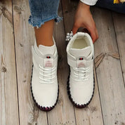 Scarpe da donna bianche invernali, suola antiscivolo, lacci, dettagli tricolore, indossate su pavimento in legno. Moda calzature casual.