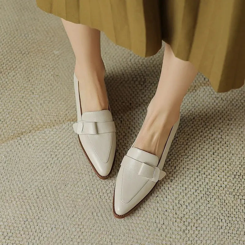 Scarpe mocassini donna in pelle bianca, design elegante con fiocco, su tappeto beige. Calzature moda femminile, stile casual chic.