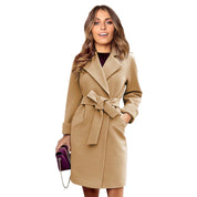 Cappotto donna beige elegante con cintura, tasche laterali, abbinato a borsa viola. Moda autunnale, abbigliamento femminile chic.