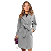 Cappotto donna grigio elegante con cintura, tasche laterali, abbinato a borsa viola. Moda autunnale, abbigliamento femminile chic.