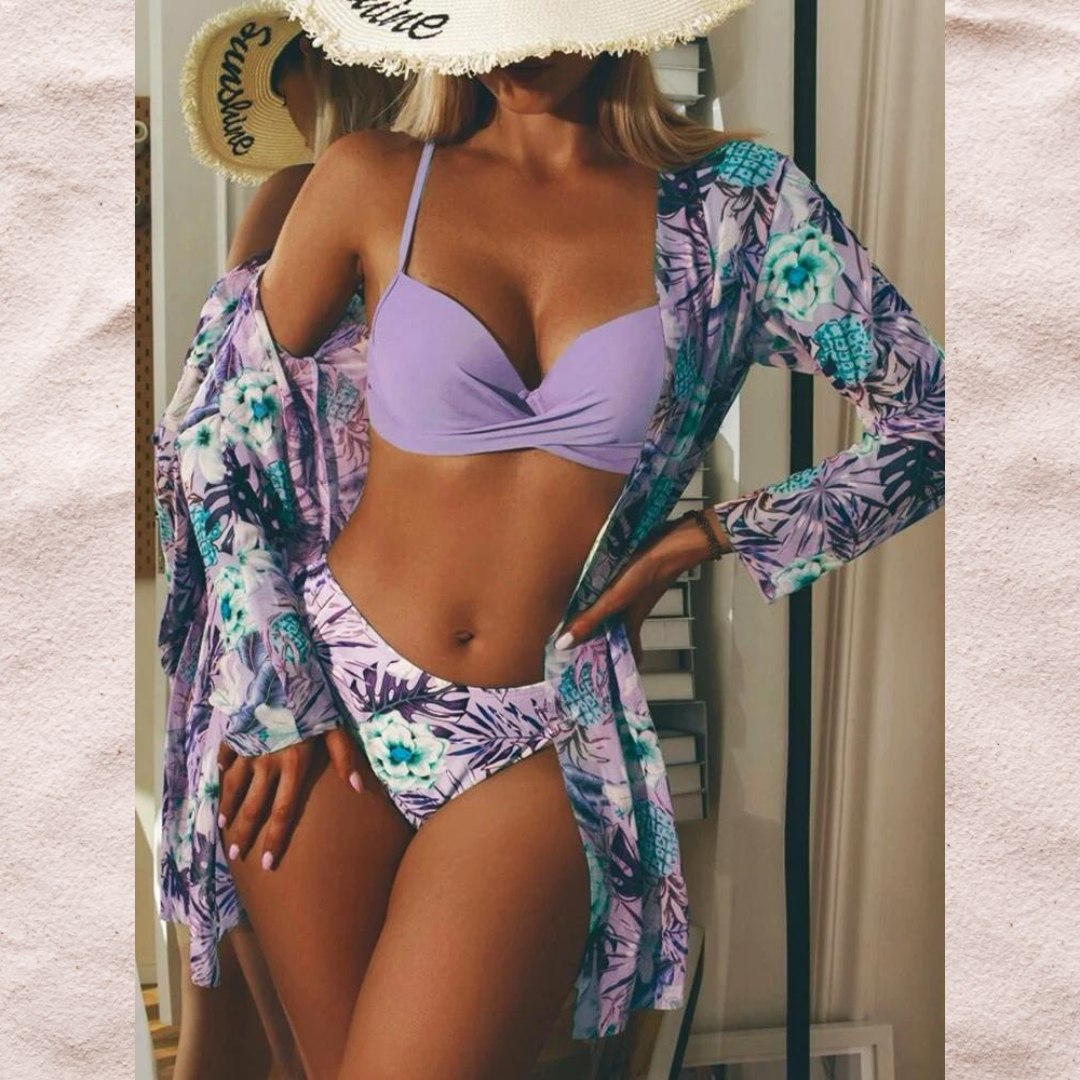 Donna in bikini viola con copricostume floreale, specchio sullo sfondo, cappello di paglia. Moda mare estiva, abbigliamento da spiaggia elegante.