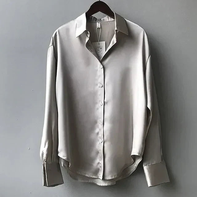 Camicia di seta grigia da donna, maniche lunghe, colletto classico, bottoni frontali, elegante e raffinata, appesa su gruccia.