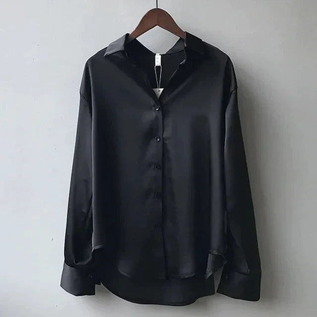 Camicia nera in raso lucido da uomo, maniche lunghe, colletto classico, bottoni frontali, elegante e moderna, appesa su gruccia di legno.