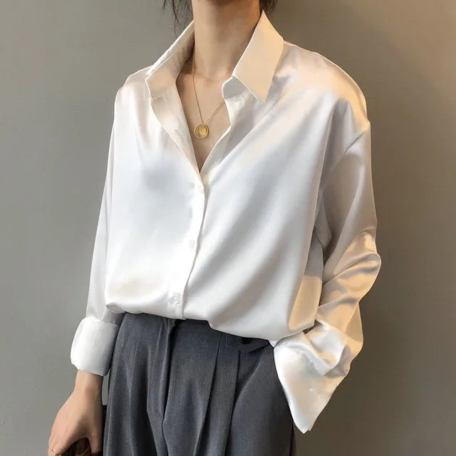 Camicia bianca in seta lucida, maniche lunghe, abbinata a pantaloni grigi eleganti. Look sofisticato e moderno per donna.