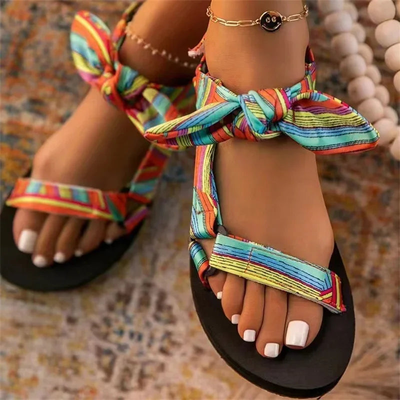 Sandali estivi colorati con fiocco, suola nera, indossati su tappeto. Accessorio alla caviglia. Scarpe moda donna, stile casual e vivace.